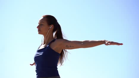 Sporty-young-woman-exercising-against-blue-sky